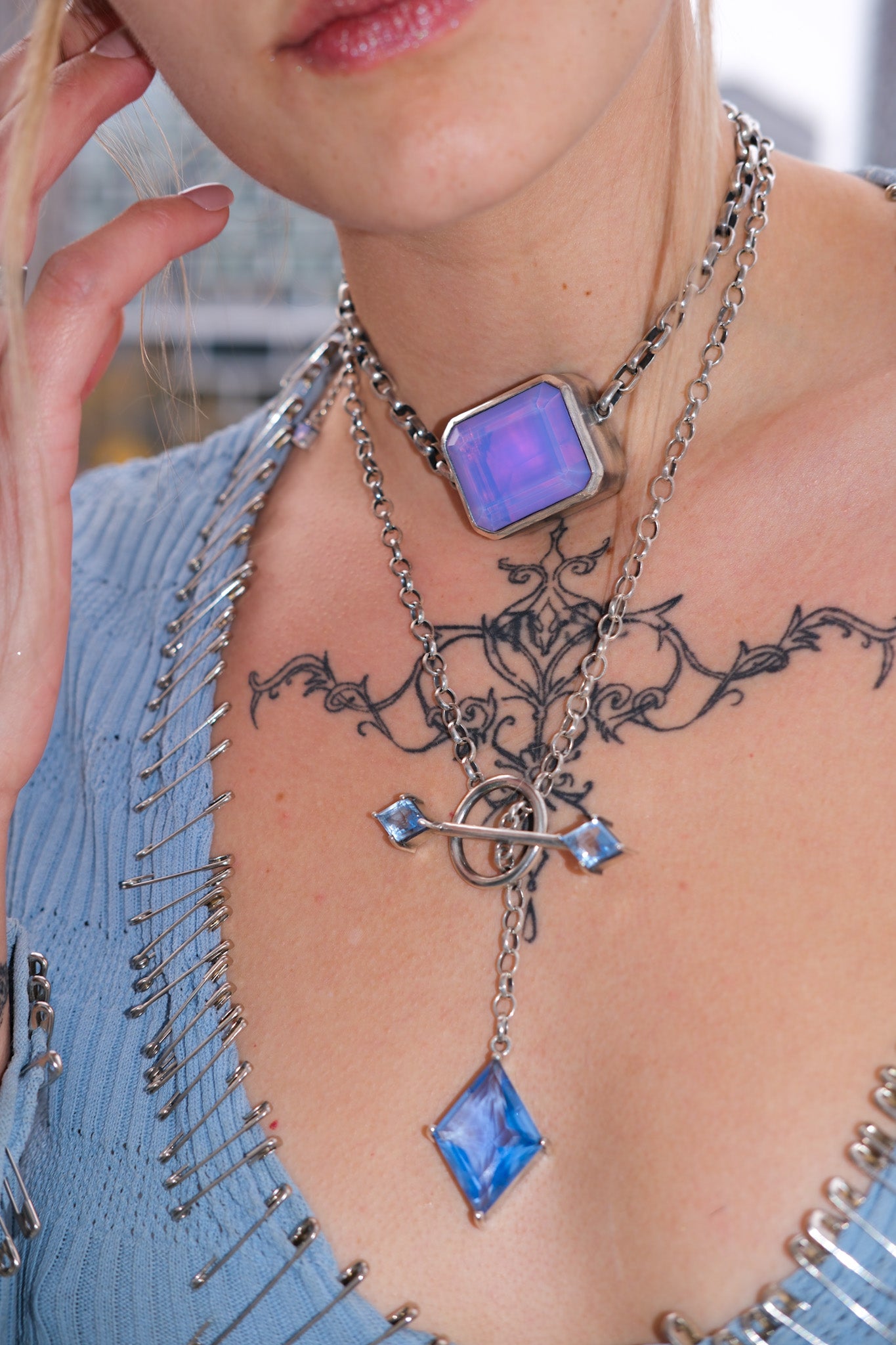 Close-up of a person wearing a detailed necklace with blue stones and a tattoo on their chest.