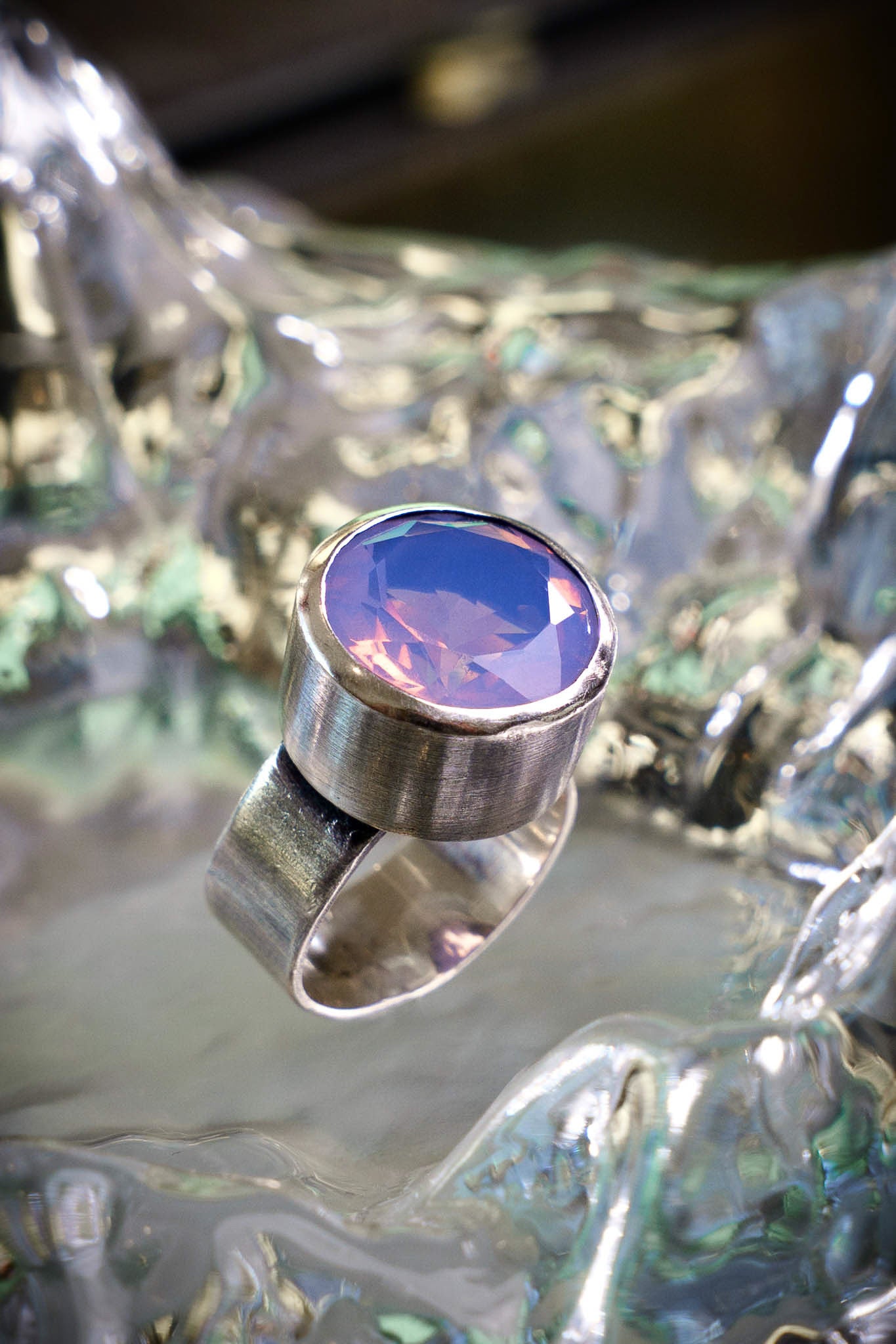 Silver ring with a colorful gemstone on a reflective surface