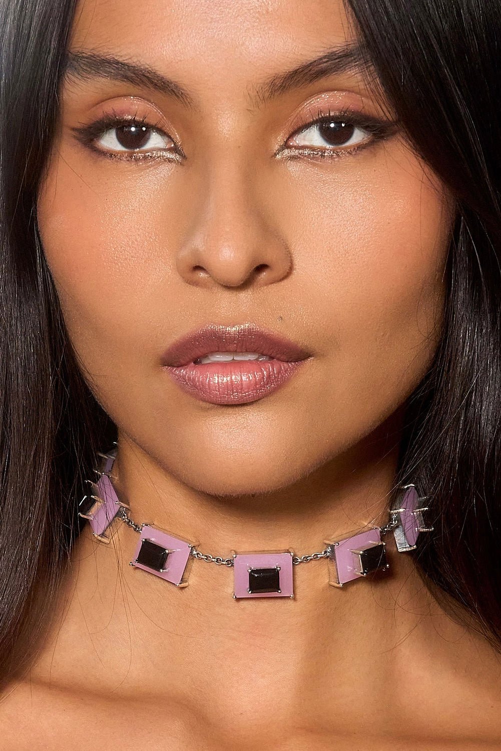 Close-up of a woman wearing a decorative necklace with pink and black stones.