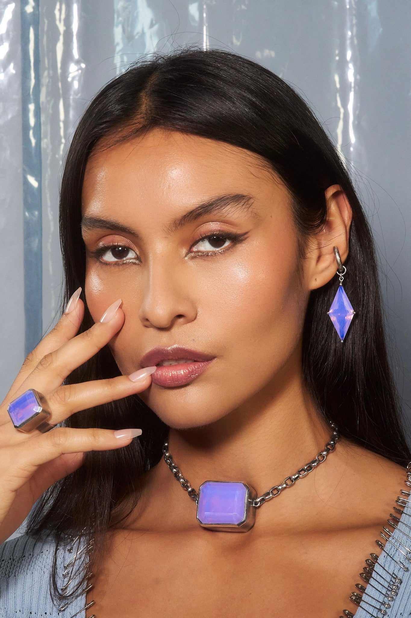 Woman wearing a necklace and earrings with a purple gemstone, posing against a gray background.