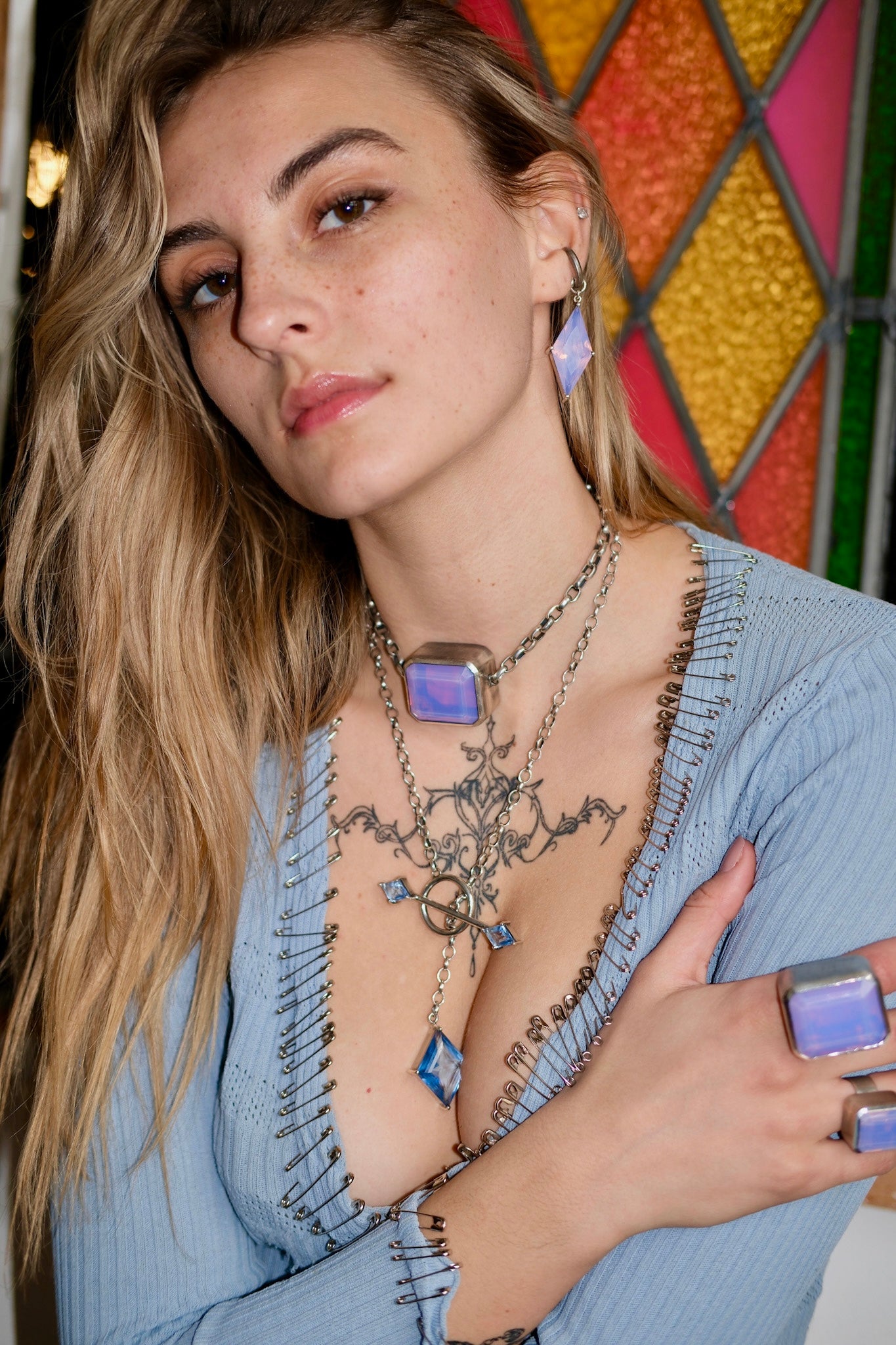 Woman wearing a blue top  and blue gemstone necklaces with a colorful stained glass window in the background