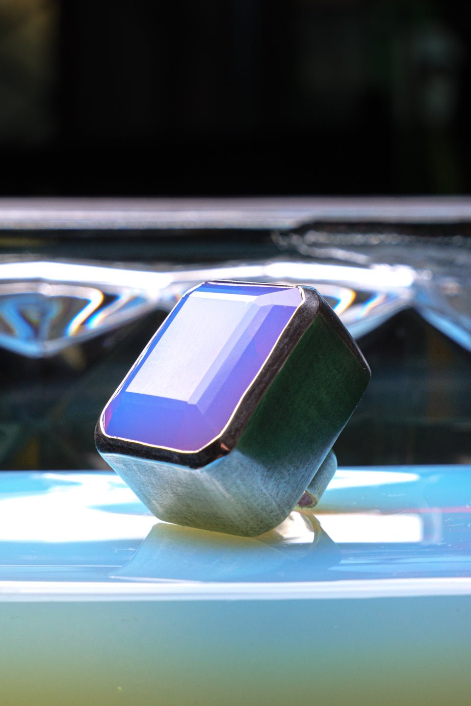 Silver ring with a lavender gemstone on a reflective surface